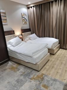 two beds in a hotel room with white sheets at بيت الجود للأجنحة المفروشة in Sīdī Ḩamzah