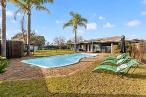 a swimming pool with two lawn chairs and palm trees at NEW - Hilderton on Hogans in Yarrawonga