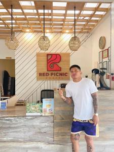 Ein Mann steht vor einem roten Picknickschild. in der Unterkunft Red Picnic Hostel in Panglao