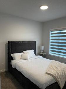 a bedroom with a bed with white sheets and a window at Brand New - Home Away from Home in NW Calgary in Calgary