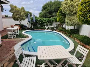 a swimming pool with two white chairs and a table at Apelles Palace Guest House in Gaborone