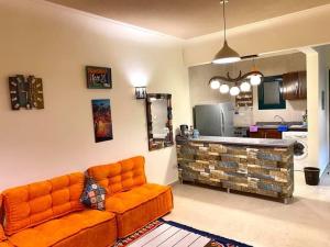 an orange couch in a living room with a kitchen at Furnished Chalet Apartment at La Hacienda Ras Sedr in Ras Sedr