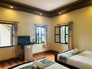 a bedroom with two beds and a flat screen tv at Villa Ban Pakham Hotel in Luang Prabang