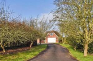 a road leading to a red house with a white garage at Boundary House Studio, Moulton in Moulton