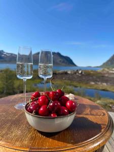 a bowl of cherries on a table with two wine glasses at Designhytte med jacuzzi sentralt i Lofoten in Kleppstad