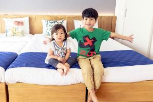 due bambini piccoli seduti su un letto di Chura Minpaku Ishigaki a Isola di Ishigaki