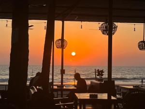 Ein Mann, der bei Sonnenuntergang an einem Tisch am Strand sitzt. in der Unterkunft Jardim a Mar in Agonda