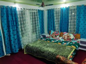 a bedroom with blue curtains and a bed with a comforter at Rose Bowl Guest House Homestay in Bāgh Chandpura