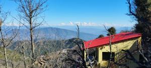 a house with a red roof with mountains in the background at Ababeel Homestay, Hartola in Rāmgarh