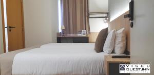 um quarto de hotel com uma cama com lençóis brancos e almofadas em Viseu Guest Inn em Viseu