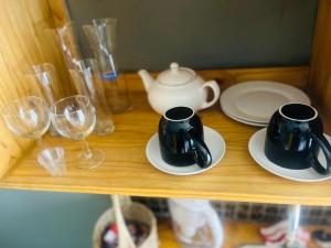 two cups and plates on a shelf with wine glasses at Bird Song in Roodepoort