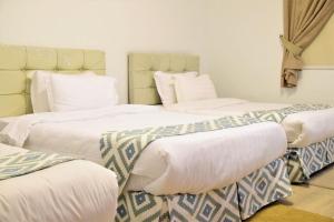 3 Betten in einem Zimmer mit weißer Bettwäsche und Kissen in der Unterkunft فاوتشر فان بيتش in Durrat Al-Arus