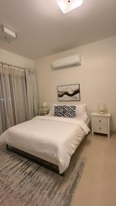 a white bedroom with a large bed and two tables at City Gem - Qurm in Muscat