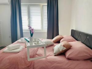 a bed with pink sheets and pillows with a table on it at Apartment Zara Bihac in Bihać