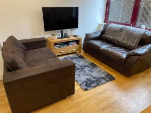 a living room with two leather couches and a flat screen tv at Home comfort 4 mins from Gatwick! in Horley