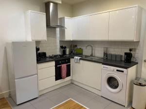 a kitchen with white cabinets and a washing machine at Home comfort 4 mins from Gatwick! in Horley