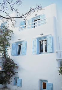 a white building with blue windows and a tree at NISOS Home Stay in Mikonos