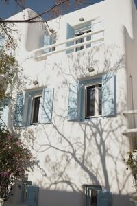 a white building with blue windows and a tree at NISOS Home Stay in Mýkonos City