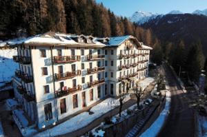 duży biały budynek z śniegiem na ziemi w obiekcie Palace Pontedilegno Resort w mieście Ponte di Legno