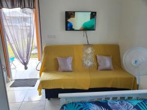a yellow couch in a living room with a tv at Bungalow vacances in Sainte-Rose