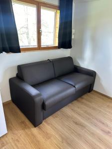 czarna skórzana kanapa w pokoju z dwoma oknami w obiekcie Tiny house détente nature la maison du pêcheur w mieście Pulligny