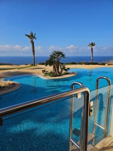 a resort swimming pool with palm trees and the ocean at CSB Apartment in Żebbuġ