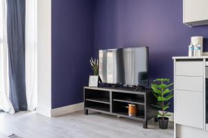 a tv on a stand in a room with a purple wall at Hemel Apartments - Lilac Luxe in Hemel Hempstead