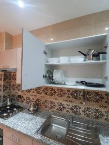 a kitchen with a sink and shelves with dishes at Appartement Maghrib Jadid in Larache