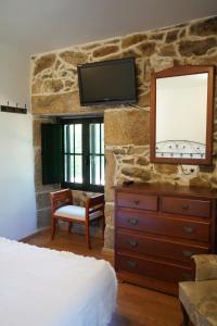 ein Schlafzimmer mit einer Kommode und einem TV an einer Steinmauer in der Unterkunft Casa Videira - Hotel rural cerca del mar in Bueu