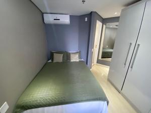 a small bedroom with a green bed and a refrigerator at Flat Moema Jamaris in São Paulo