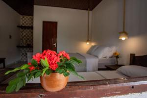 a vase with red flowers on a table in a bedroom at EcoPousada Pico do Jabre in Matureia