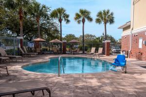 a swimming pool with a blue chair and palm trees at Comfort Inn & Suites Patriots Point in Charleston