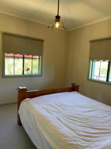 1 dormitorio con 1 cama blanca y 2 ventanas en Relaxing & beautiful Miner's cottage near Wilson’s Prom, en Foster
