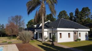 Una casa blanca con una palmera detrás. en HERMOSA CASA EN BARRIO CERRADO, A 30 KM DE LA CIUDAD DE BUENOS AIRES Y 10 KM. DEL AEROPUERTO INTERNACIONAL DE EZEIZA en Ezeiza