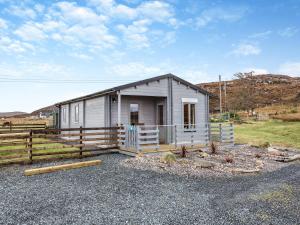 una pequeña casa gris con una valla alrededor en Seashell Lodge, en Gairloch