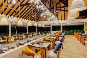 een restaurant met houten tafels, stoelen en verlichting bij Cinnamon Hakuraa Huraa Maldives - All Inclusive in Meemu Atoll
