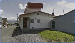 a white house with a brown door on a street at わらしべハウス in Furano