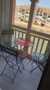 una mesa roja y 2 sillas en el balcón en Studio cabine au barcares, en Le Barcarès
