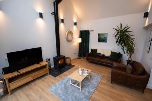 a living room with a flat screen tv and leather furniture at Forest Corner Luxury Home with Hot Tub in North Ballachulish