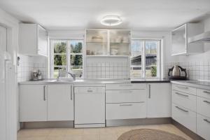 una cocina blanca con armarios blancos y ventanas en Charmerende landsted med privat skov, en Bjergby