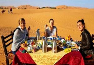 Merzouga Luxurious Camp في مرزوقة: ثلاث نساء جالسات على طاولة في الصحراء
