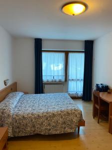 a bedroom with a bed and a desk and windows at Garní Ladinia in Pescul