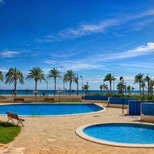 una piscina con palmeras y el océano en Beachfront Nautical Apartment, en Benimagrell