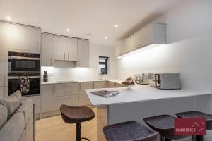 una cocina con armarios blancos y una barra con taburetes en Wokingham - 2 Bedroom - Refurbished 1st Floor Flat, en Wokingham