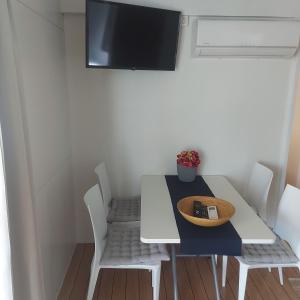 einen Esstisch mit weißen Stühlen und einen TV an der Wand in der Unterkunft Mobile home Jezera Murter Comfort in Jezera