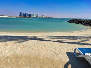 un banco sentado en una playa con una ciudad en el fondo en Marjan Island Beautiful Apartment Sea View Beach Luxury Rooms Ras Al Khaimah UAE, en Ras al Khaimah