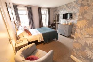 a bedroom with a bed and a chair and a tv at Wyndgrove House in Seahouses