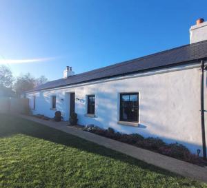 une maison blanche avec une cour gazonnée devant elle dans l'établissement Croft Cottage by Mourne Homestays, à Glasdrumman