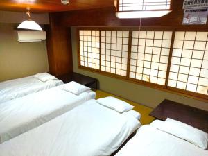 three white beds in a room with windows at Osaka Guesthouse Sakura in Osaka