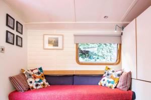 a red couch in a tiny house with a window at Slash Arts houseboat on secluded mooring in central London in London